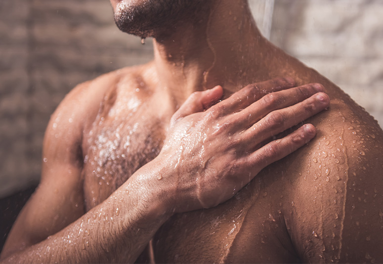 Brust bis Kinn eines Mannes von vorne unter der Dusche. Rechter Hand auf Schulter.